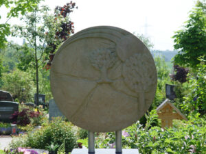 Großes rundes Ornament, das mit zwei Säulen auf einem Grabstein steht und die Sonne sowie Bäume zeigt