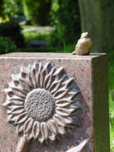 Brauner Grabstein mit einer Sonnenblume als Ornament und einem Bronzevogel