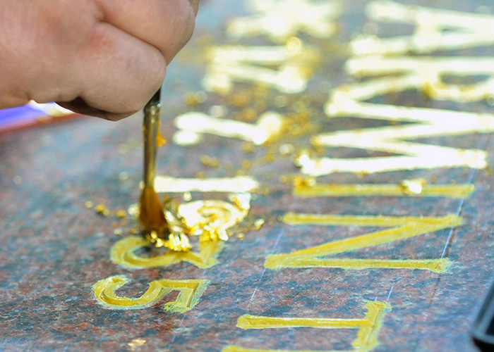 Goldfolie wird mit Pinsel auf einen Grabstein-Schriftzug aufgebracht