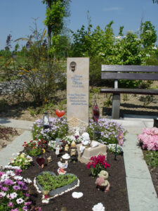 Grab eines Sternenkinds mit Sandstein-Grabstein und kleiner Bronzefigur