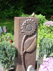 Grabstein-Säule mit großer Sonnenblume als Ornament und Bronze-Vogel
