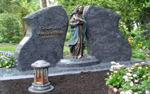 Grabmal bestehend aus zwei Steinen und einer Bronzefigur und einer Kerze